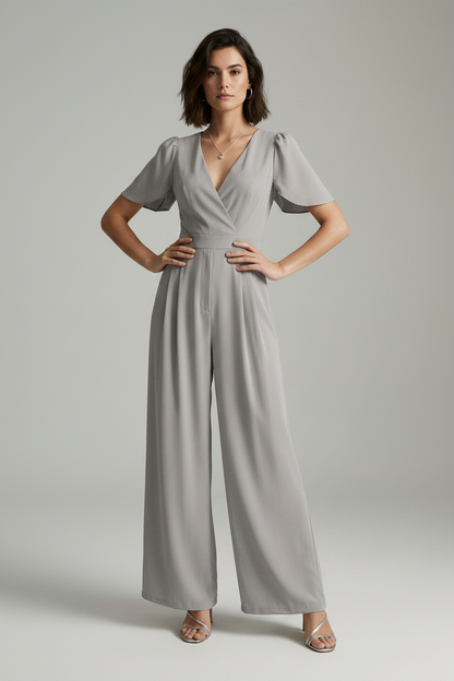 A woman modeling a light gray jumpsuit with short puff sleeves, a wrap-style V-neck bodice, and wide legs, photographed against a plain light gray studio background.