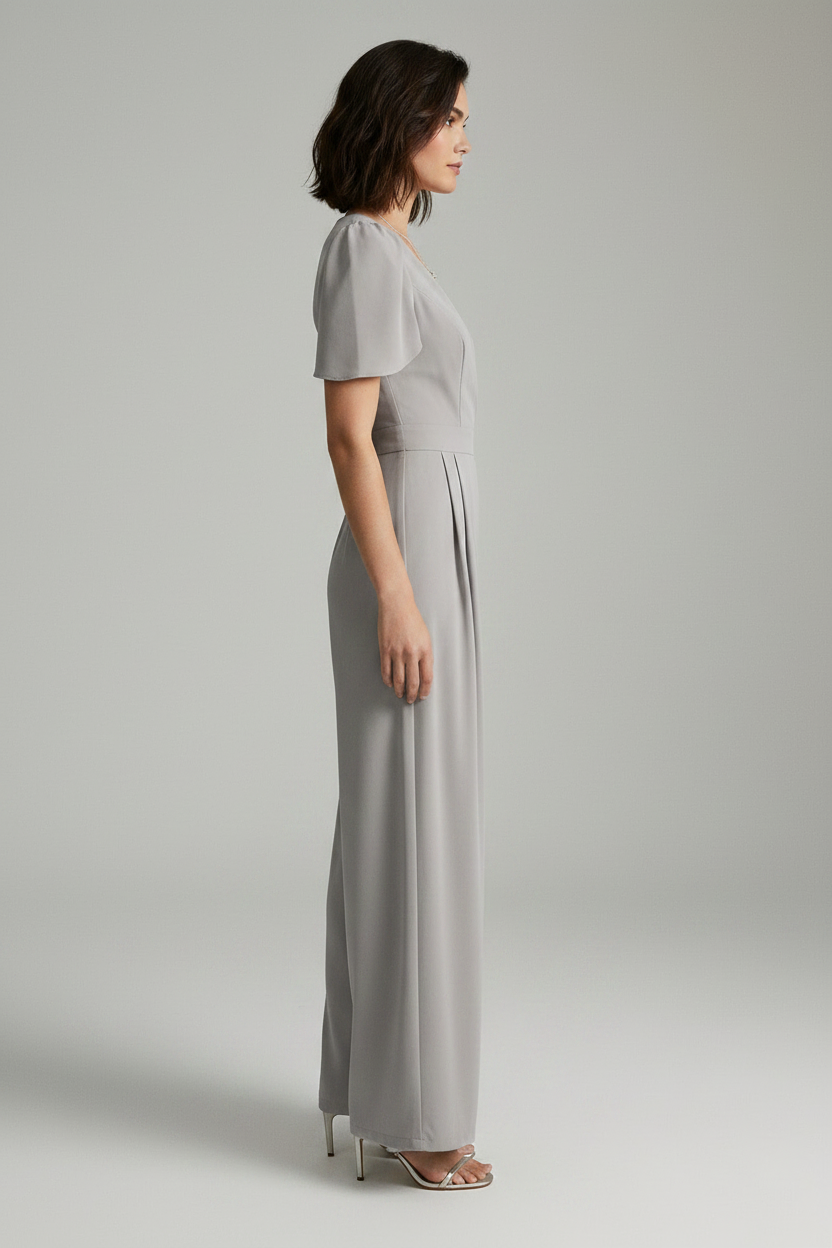 A woman modeling a light gray jumpsuit with short puff sleeves, a wrap-style V-neck bodice, and wide legs, photographed against a plain light gray studio background.