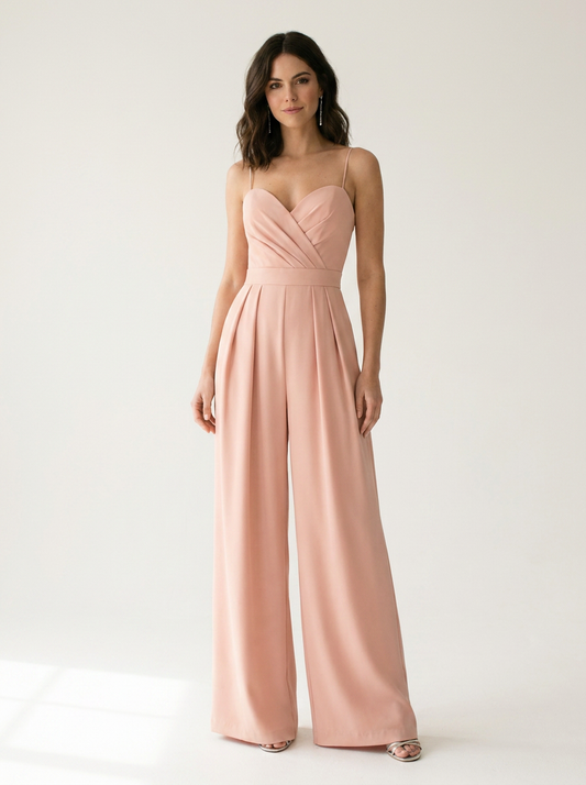 A woman modeling a dusty pink wide-leg jumpsuit with thin spaghetti straps and a sweetheart neckline, standing against a clean white studio background.
