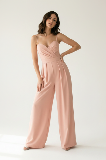 A woman modeling a dusty pink wide-leg jumpsuit with thin spaghetti straps and a sweetheart neckline, standing against a clean white studio background.