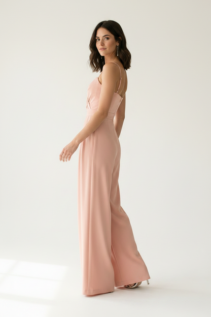A woman modeling a dusty pink wide-leg jumpsuit with thin spaghetti straps and a sweetheart neckline, standing against a clean white studio background.