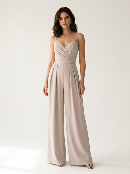 A woman modeling a light beige wide-leg jumpsuit with spaghetti straps and a sweetheart neckline, standing against a clean white studio background.