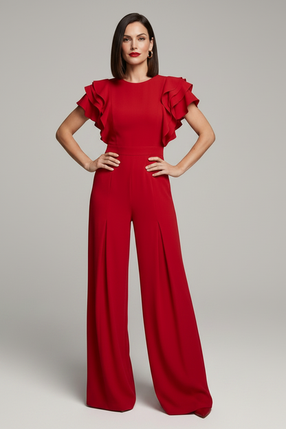 A woman modeling a bright red wide-leg jumpsuit with ruffled short sleeves, standing against a neutral light gray studio background.