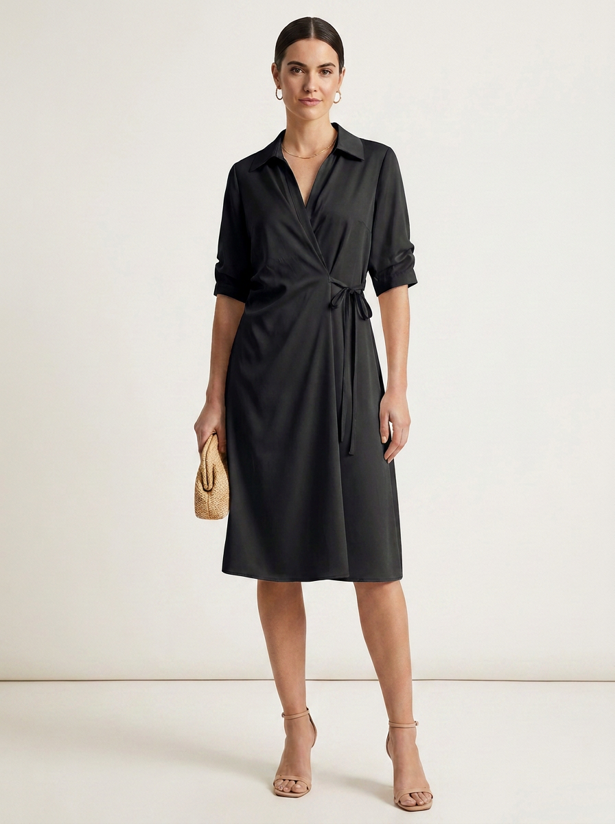 A woman modeling a black wrap-style midi dress with a collar, three-quarter sleeves, and a self-tie waist, standing against a plain light studio background. She is holding a small beige woven clutch and wearing nude high-heel sandals.